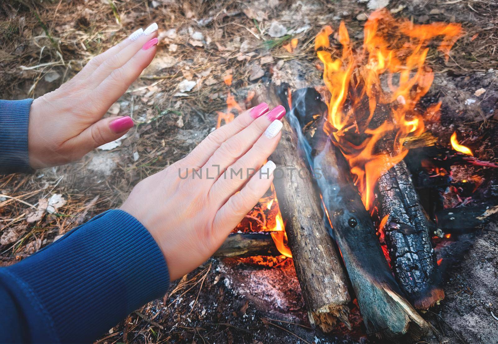 woman is making fire while camping outdoors at the forest - warming up her hands near the fire by Nickstock