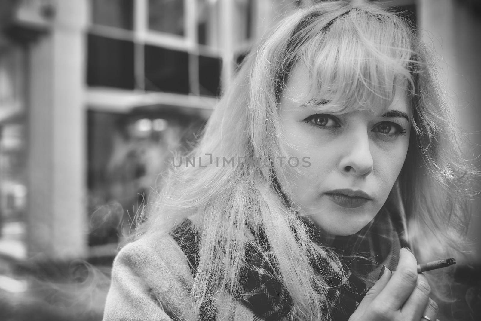 Woman in a very bad mood, holding in his hand, holding a smoldering between his fingers fuming cigarette. Cigarette close-up. black and white by Nickstock