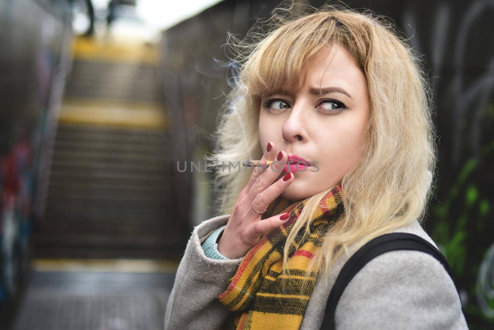 serious young blond woman smoking a cigarette and looking Aside in underground passage