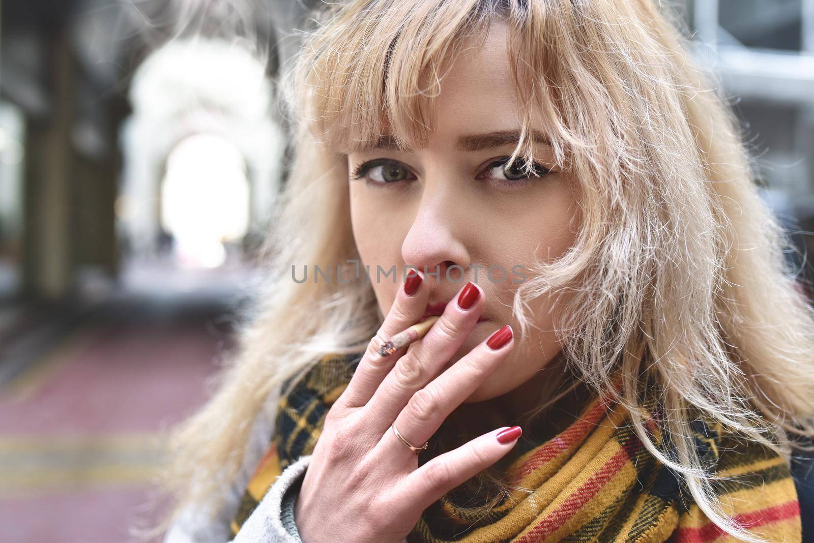 serious young blond woman smoking a cigarette and looking at camera by Nickstock