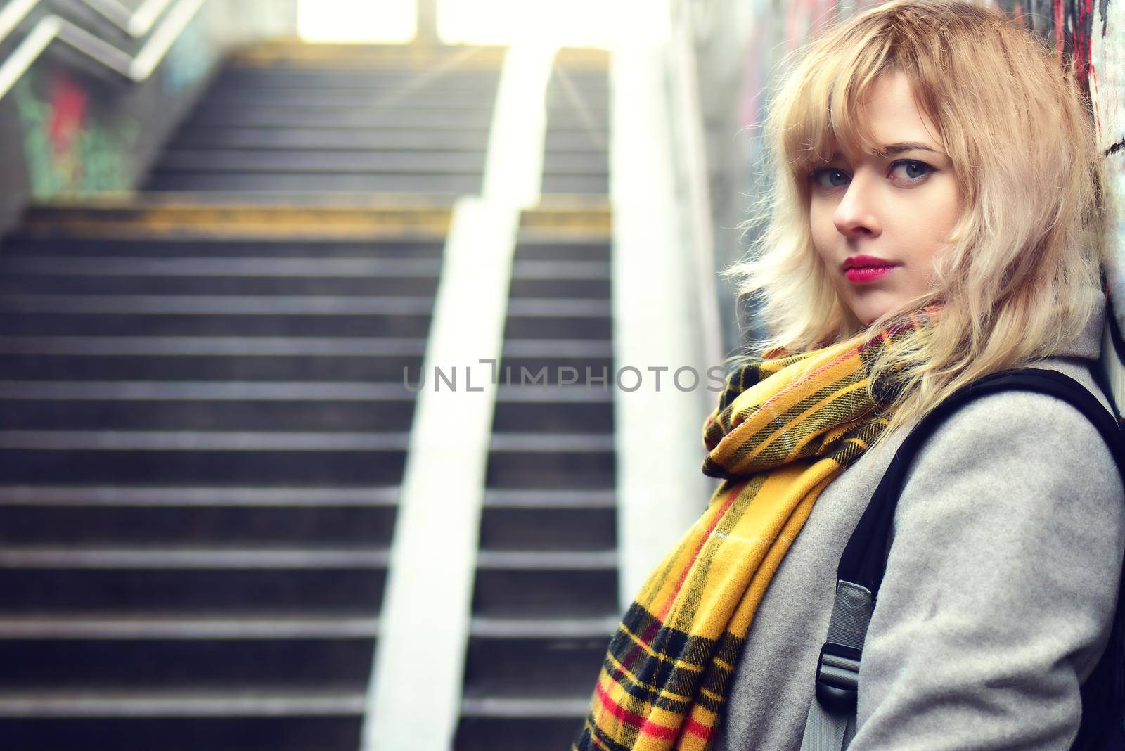Beautiful blonde girl standing near a wall with graffiti in underground passage