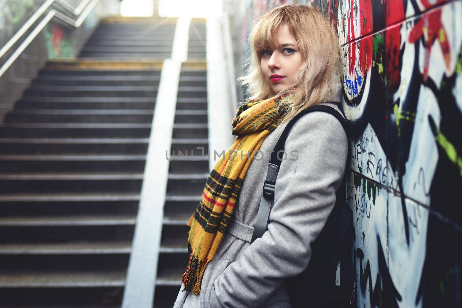 Beautiful girl standing near a wall with graffiti in underground passage by Nickstock
