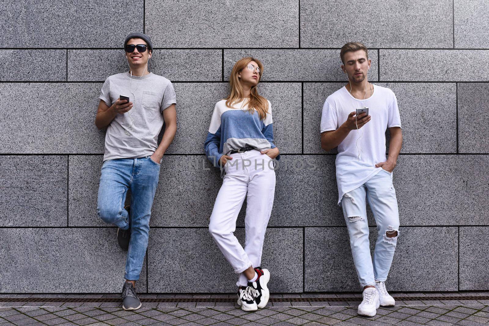 Fashion portrait of Three best friends posing at street, wearing stylish outfit and jeans against gray wall