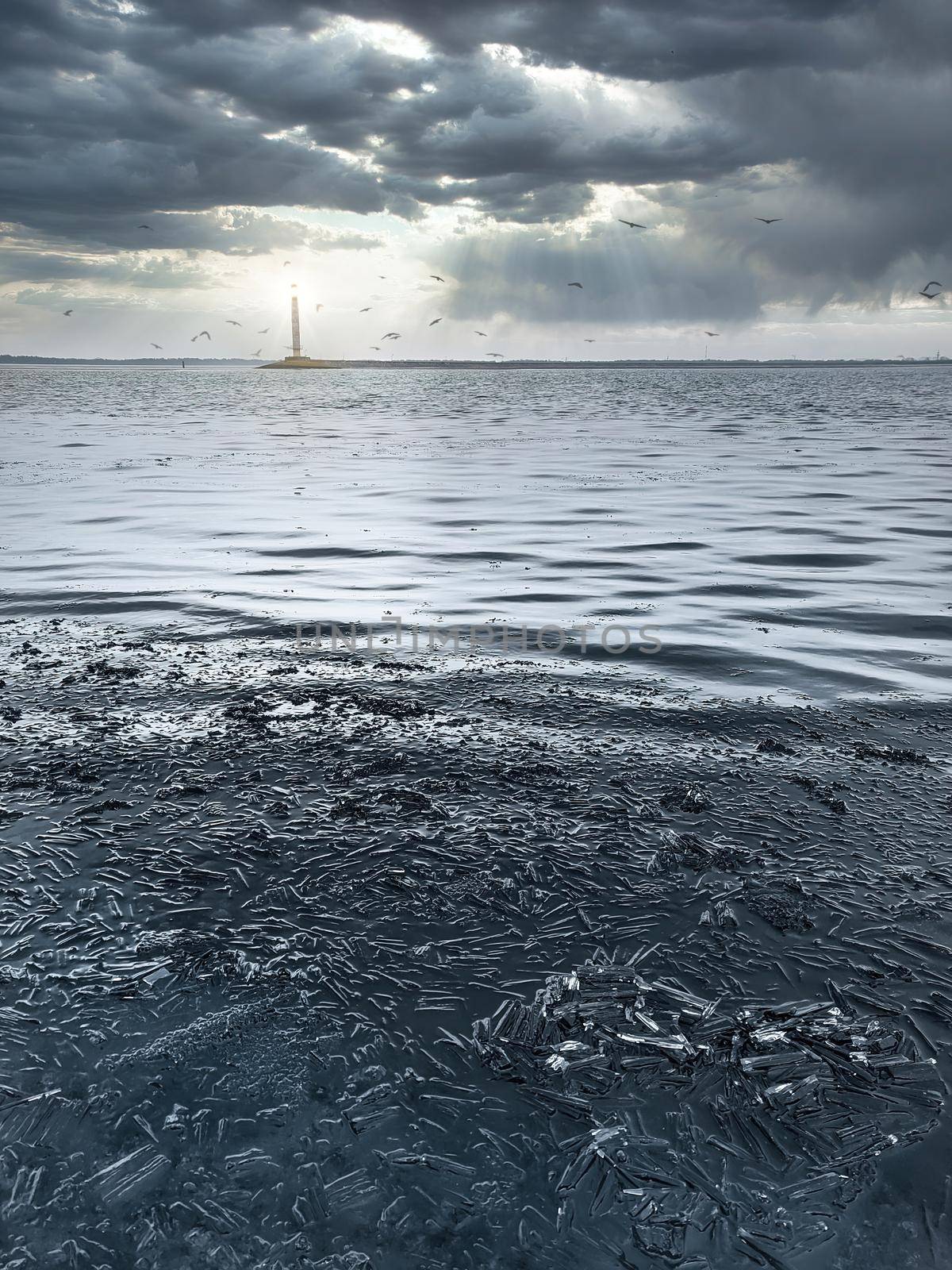 Blue winter ice a winter scene with blue ice with a lighthouse glowing in the distance, against a background of beautiful overcast clouds.