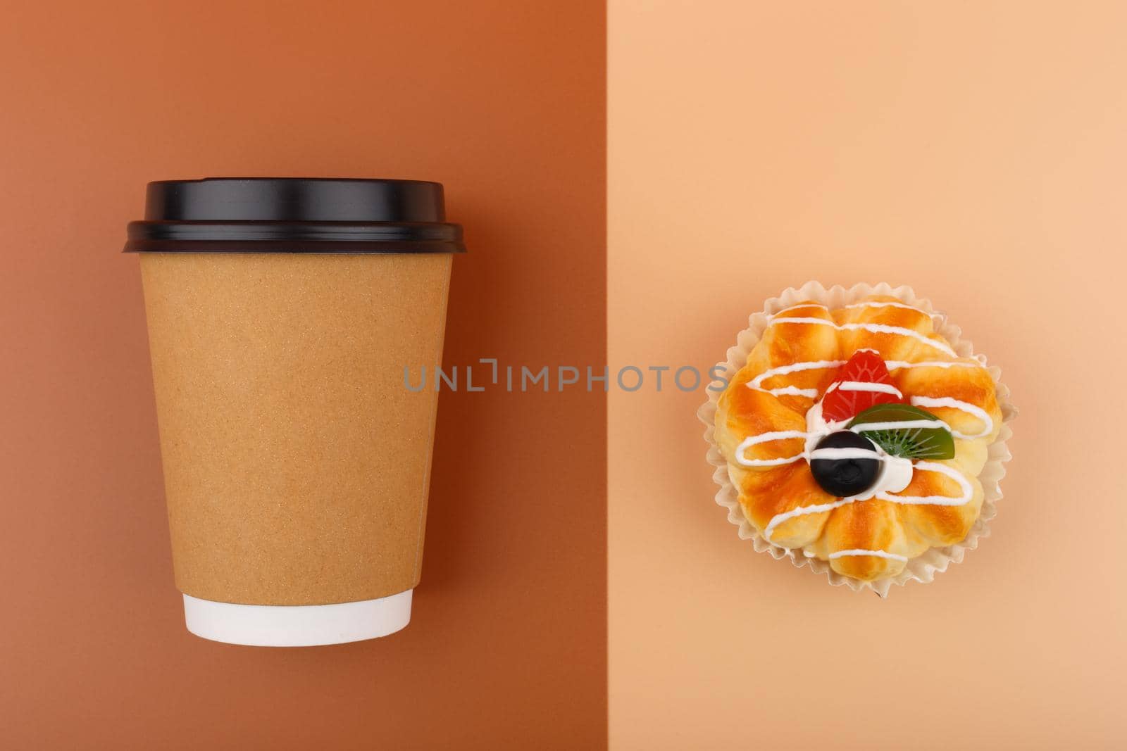 Top view of coffee or tea in brown cardboard cup with pastry against brown and beige background. Concept of hot drinks, take away food, small breaks or cheat meal