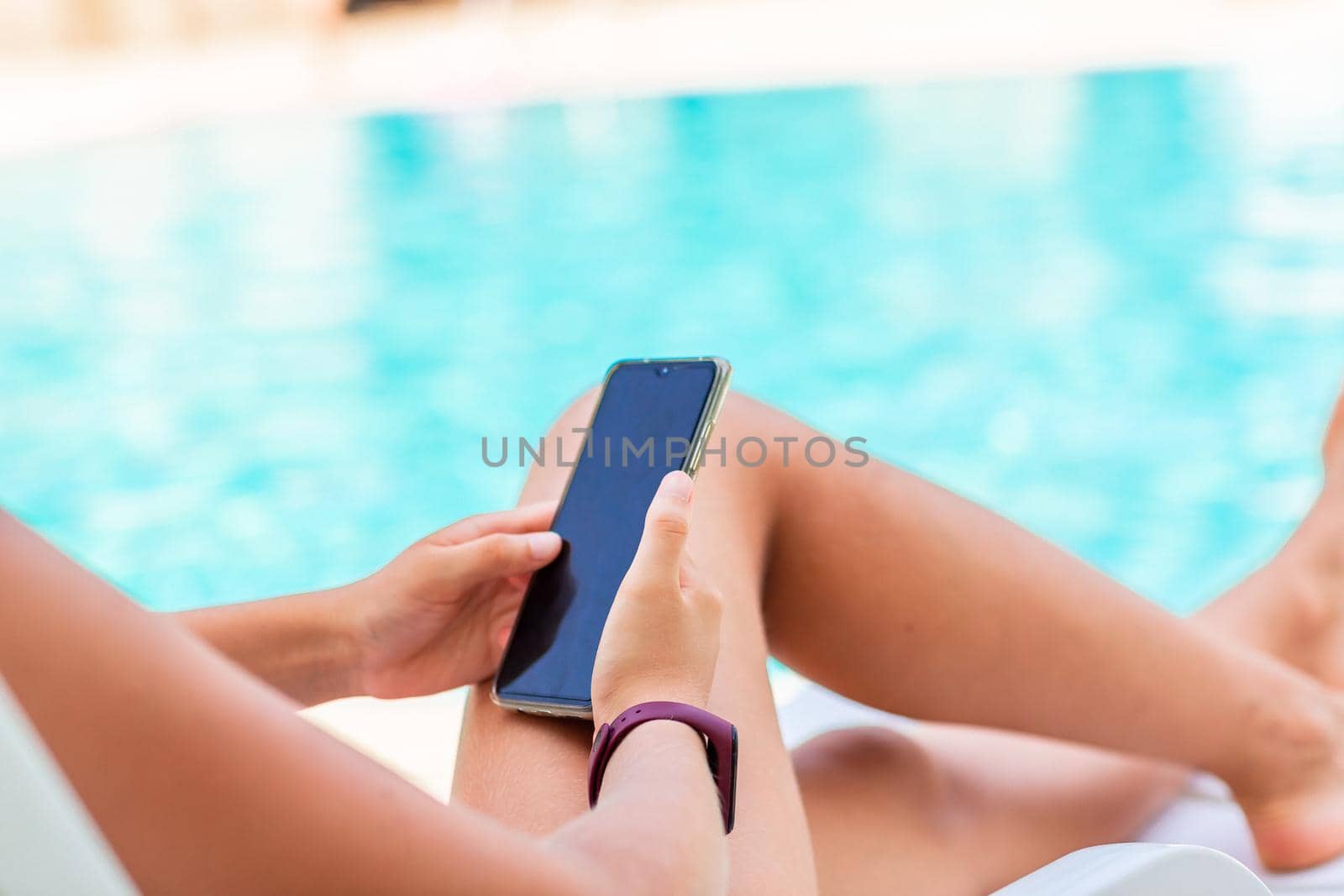 Close up of teenage girl's hands playing games and searching web on the telephone at the pool on vacation. Gadget dependency disorder problem for kids during holiday vacation at the seaside concept