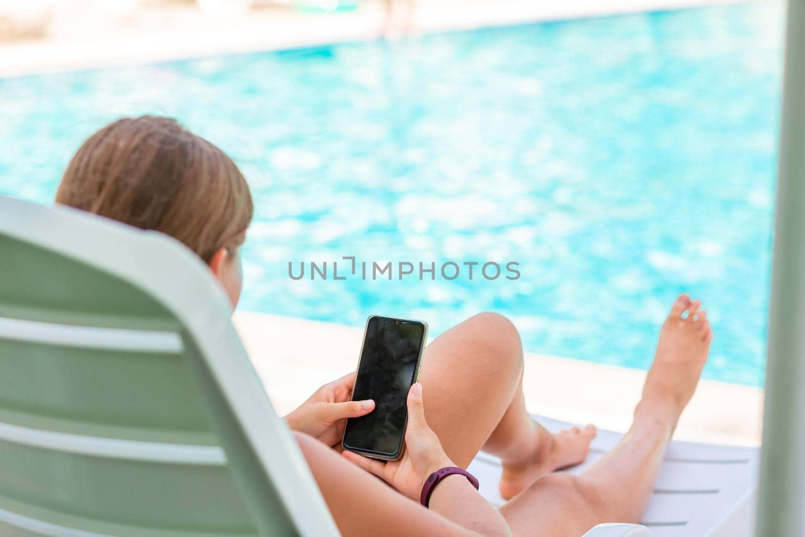 Teenage girl playing games and searching web on the telephone at the pool on vacation. Gadget dependency disorder problem for kids during holiday vacation at the seaside concept