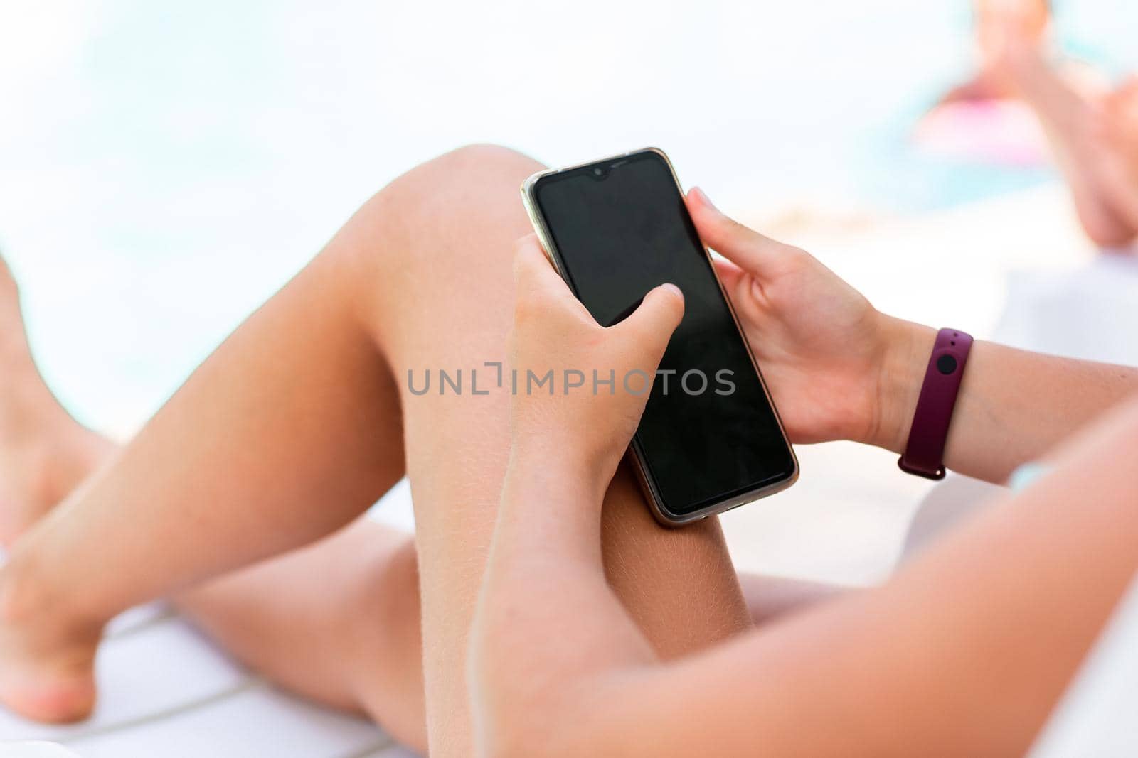 Close up of teenage girl's hands playing games and searching web on the telephone at the pool on vacation. Gadget dependency disorder problem for kids during holiday vacation at the seaside concept