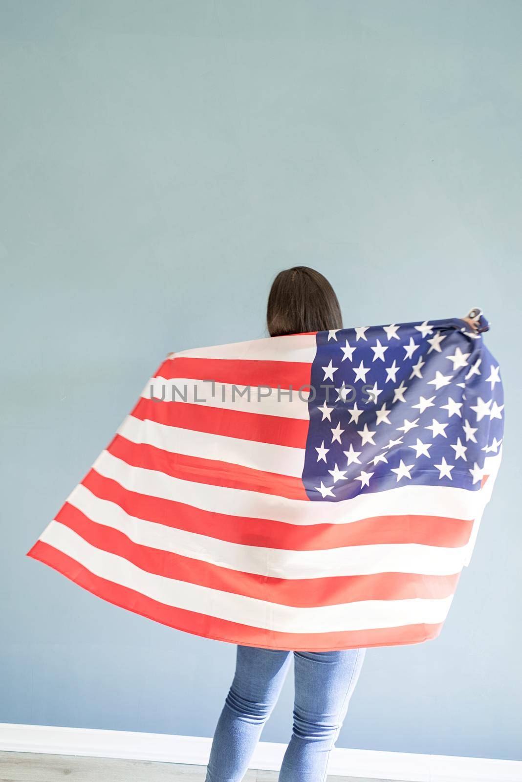 beautiful young woman with american flag on blue background, view from behind by Desperada