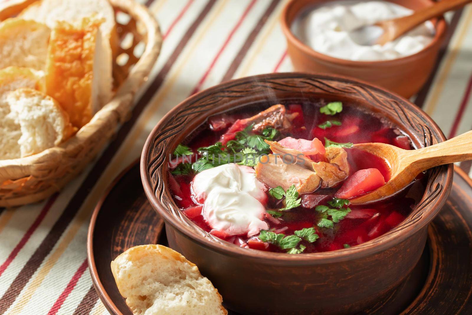 Freshly cooked hot homemade borscht - traditional dish of Russian and Ukrainian cuisine in earthenware dishes with bacon, bread, sour cream and garlic.