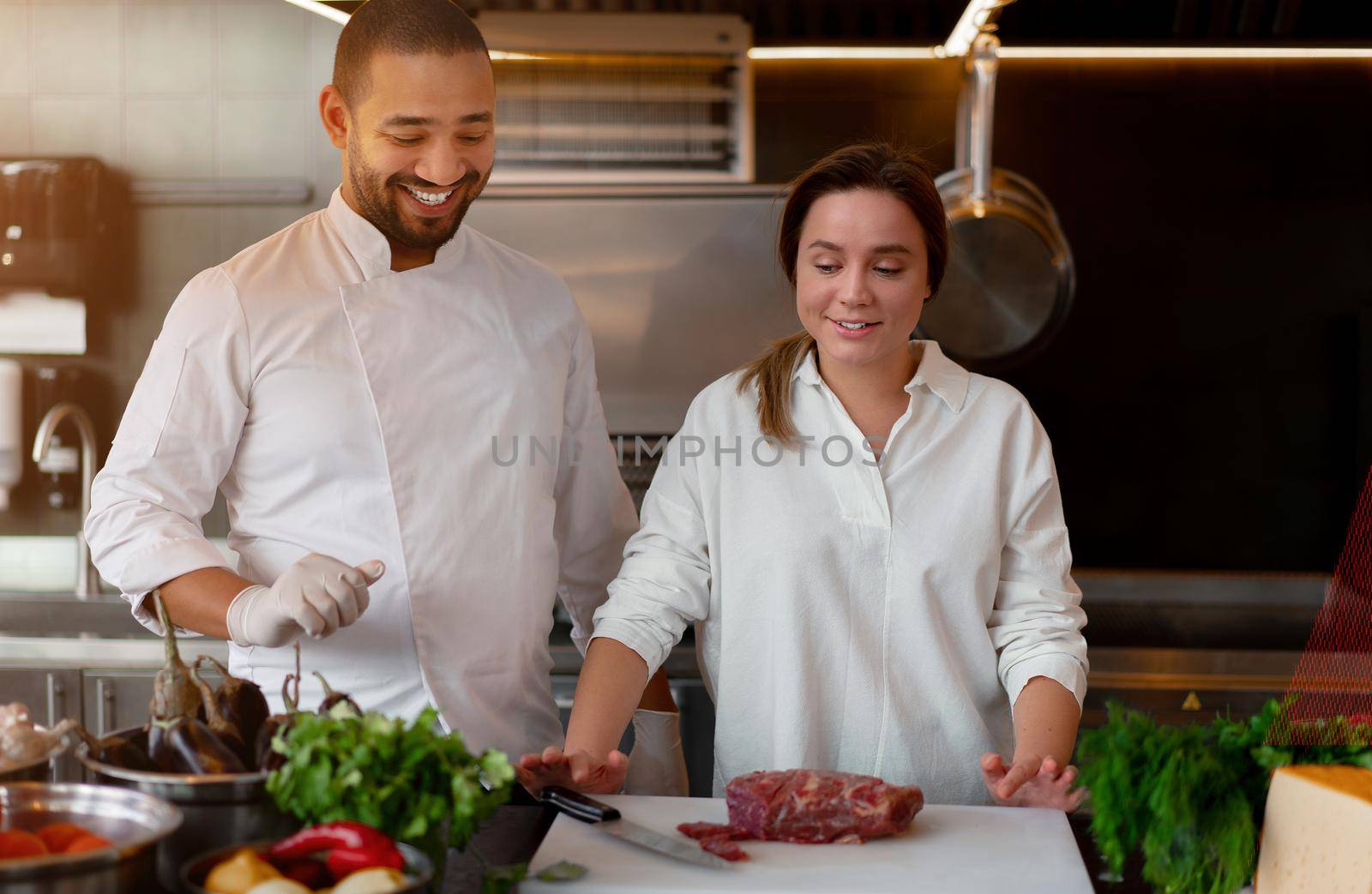 Handsome young African chef is cooking together with Caucasian girlfriend in the kitchen A cook teaches a girl how to cook. Man and woman cooking in professional kitchen. interracial relationship