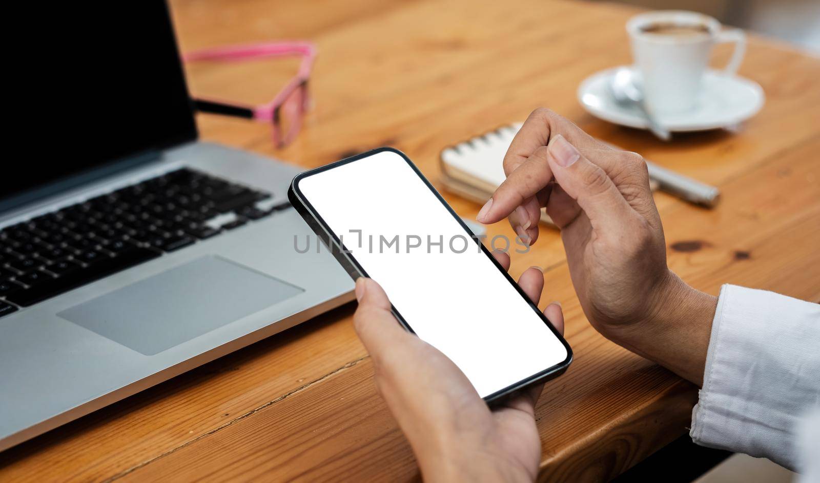 Woman hold and touching blank mobile screen for mock up with working space at cafe by nateemee