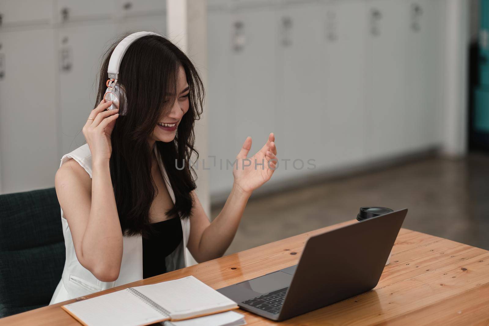 Smiling girl student wear wireless headphone study online with teacher, happy young asian woman learn language listen lecture watch webinar write notes look at laptop sit in cafe, distant education. by nateemee