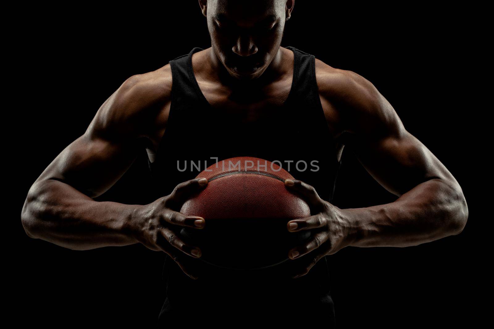 Basketball player holding a ball against black background. Serious concentrated african american man by kokimk