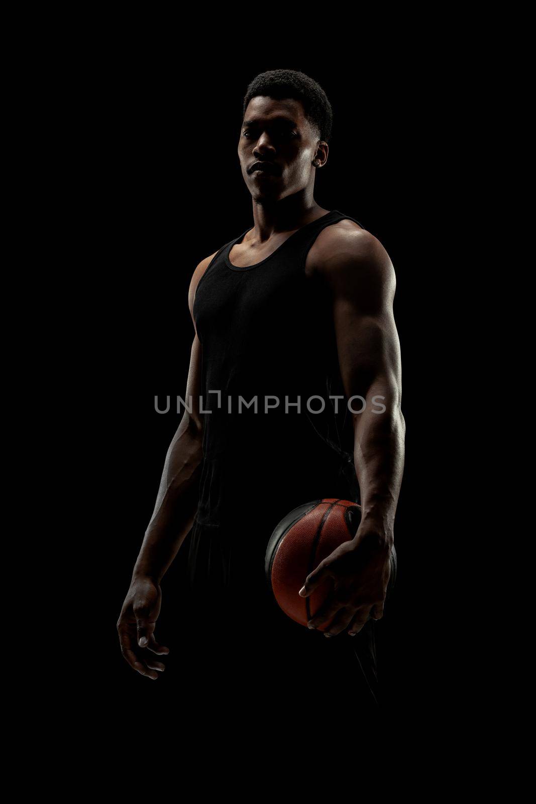 Basketball player holding a ball against black background. Serious concentrated african american man by kokimk