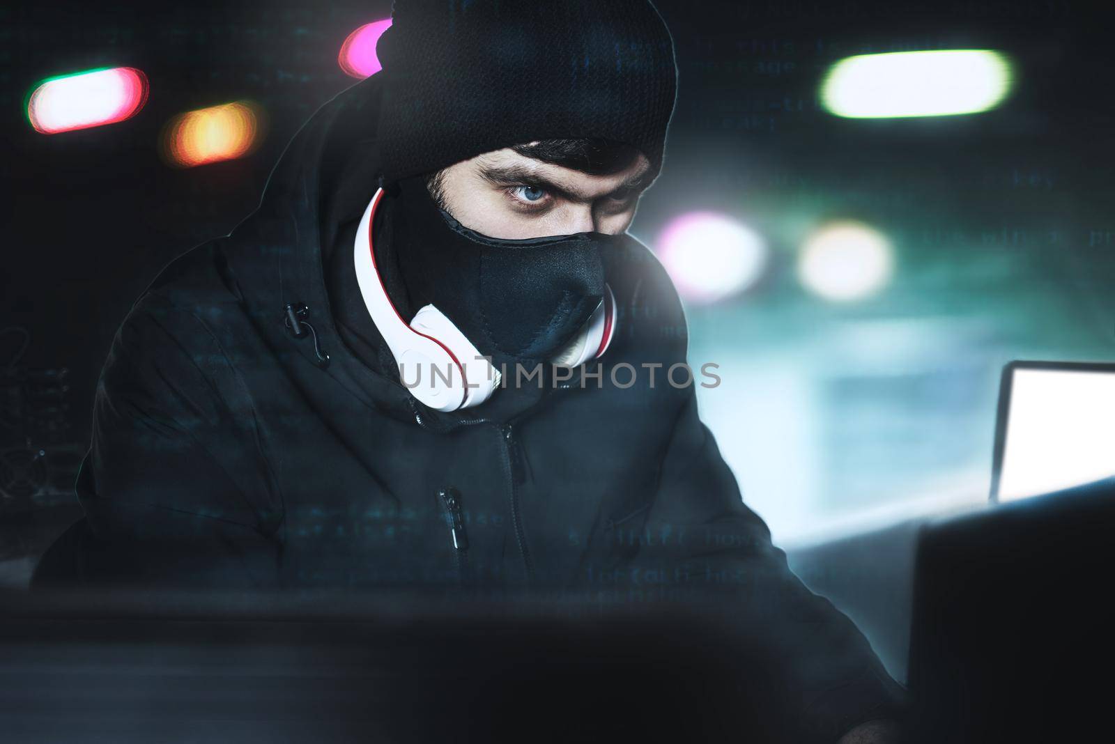 Angry computer hacker weared balaclava stealing data Via PC from His Underground Hideoutin front of black background and blue light. close portrait. hack concept