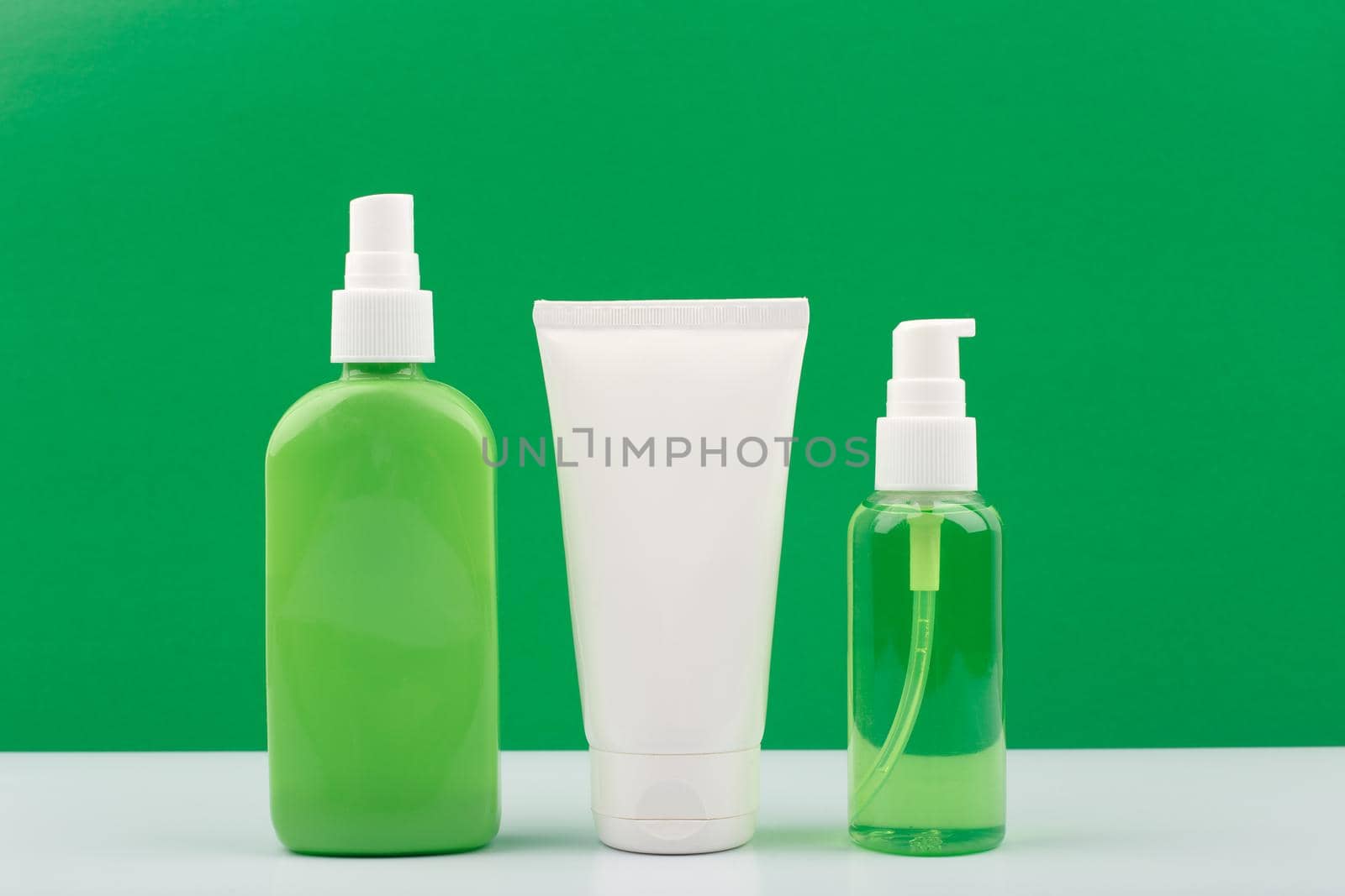 Set of green and white cosmetic bottles against yellow background. Concept of organic beauty products with natural ingredients. Moisturizing body spray, face cream and cleansing gel for face.