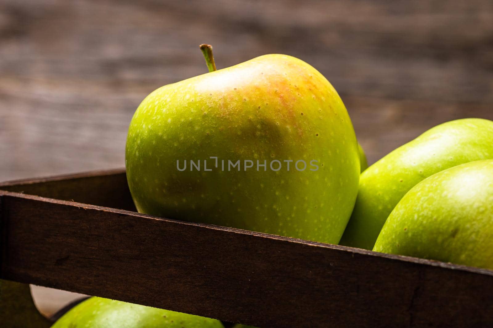 Wooden crate with ripe green apples on wooden table.