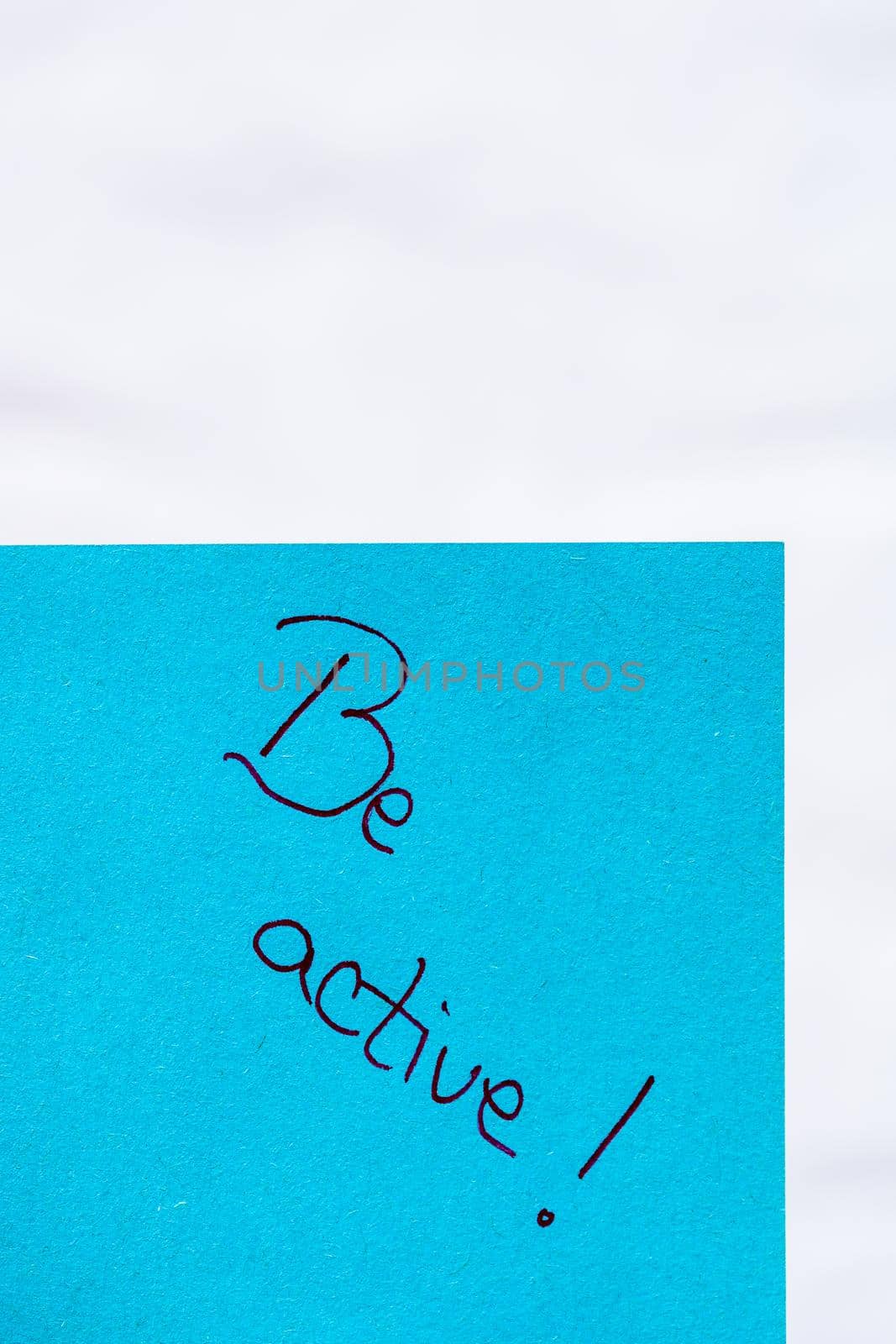 Be active handwriting text close up isolated on blue paper with copy space. Writing text on memo post reminder