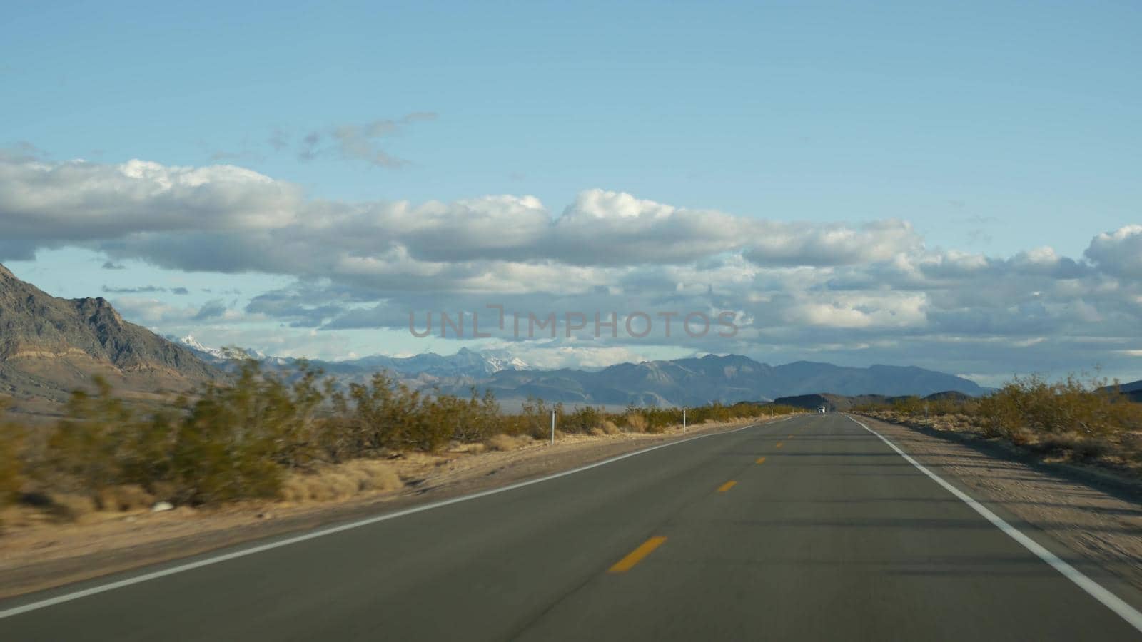 Road trip, driving auto from Death Valley to Las Vegas, Nevada USA. Hitchhiking traveling in America. Highway journey, dramatic atmosphere, clouds, mountain and Mojave desert wilderness. View from car