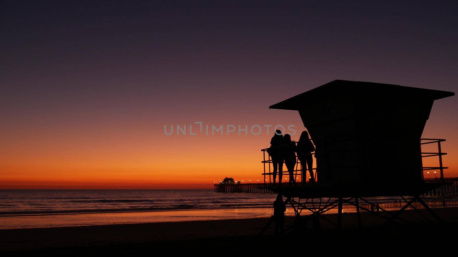 Young teen girls silhouettes, lifeguard watch tower, friends on pacific ocean beach, California USA. by DogoraSun