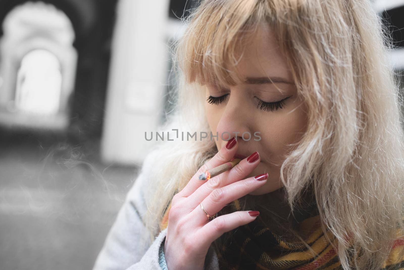 serious young blond woman on gray background , smoking with closed eyes