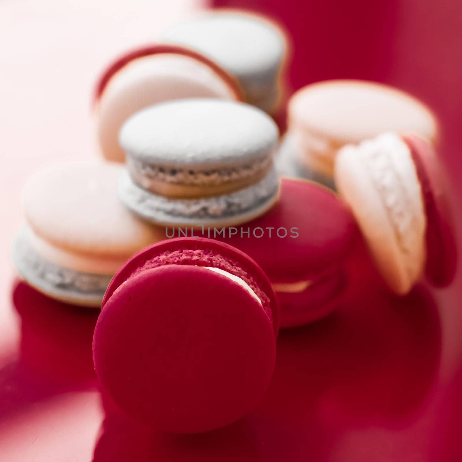 Pastry, bakery and branding concept - French macaroons on wine red background, parisian chic cafe dessert, sweet food and cake macaron for luxury confectionery brand, holiday backdrop design