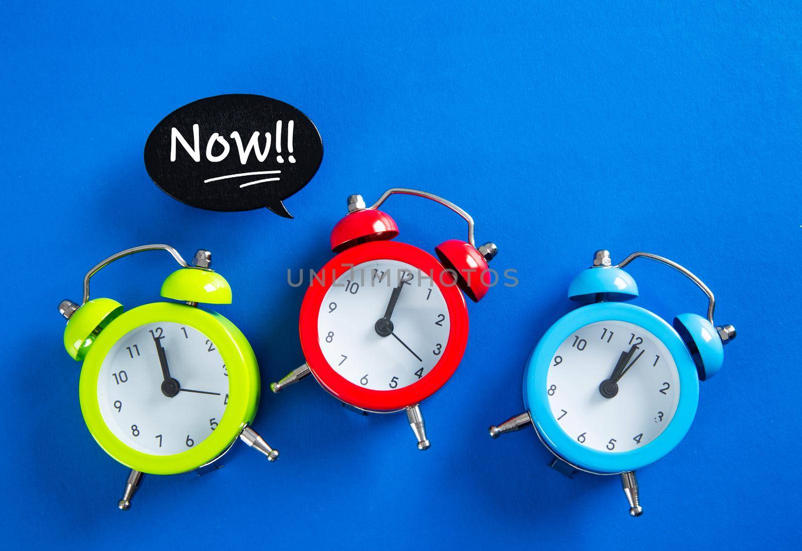 Speech bubble with  the word NOW on alarm clock on blue background with copy space using as stop procrastination, self discipline or motivation to complete task