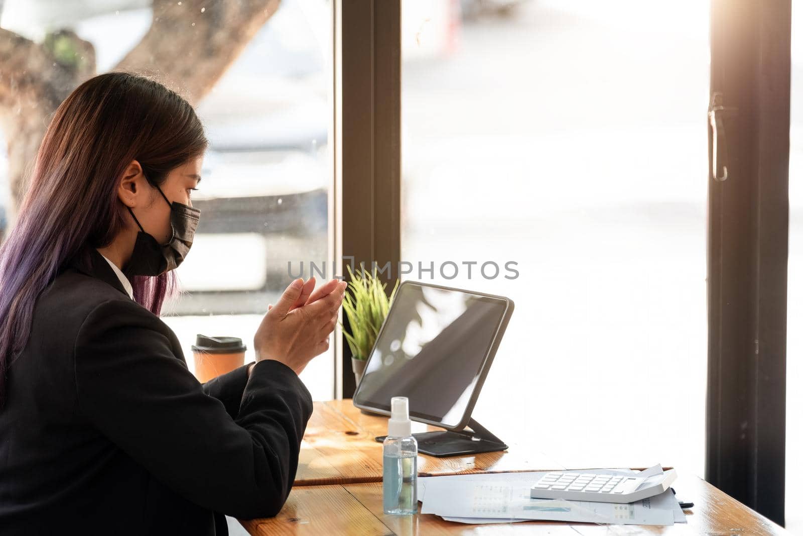 Businesswoman with face mask communicating with her colleague via video call while working in the office during COVID-19 pandemic by nateemee