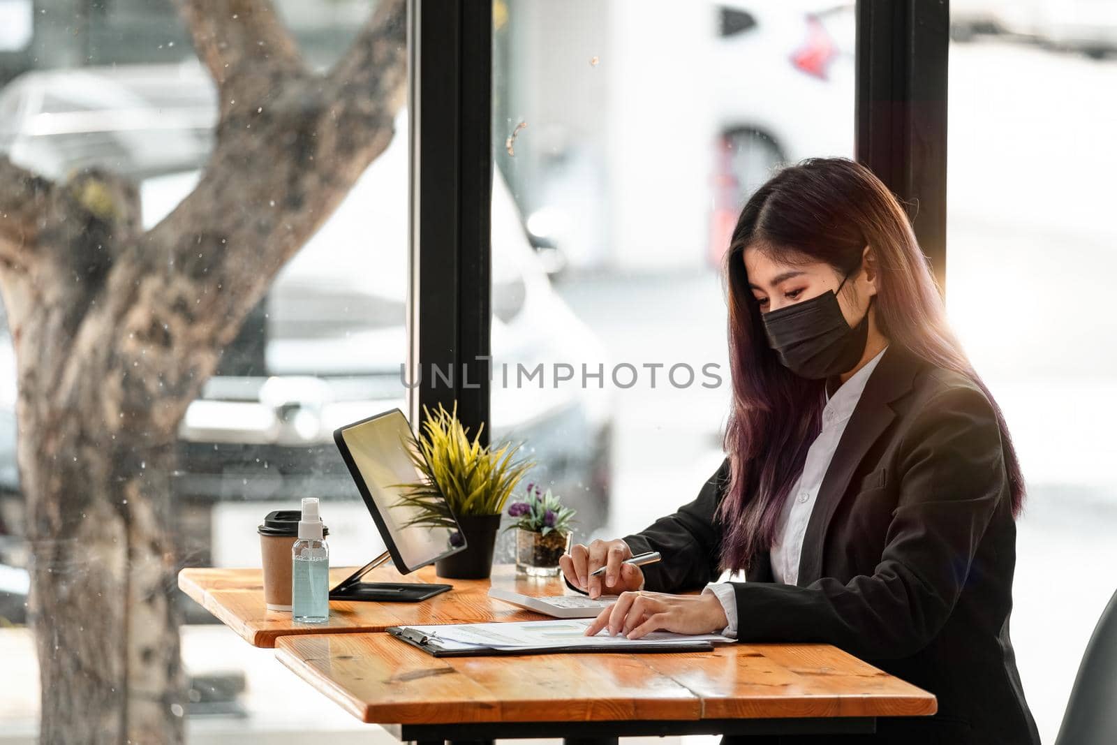 Side view of asian businesswoman wearing face mask while working on a computer in the office. hygiene and safety concept. by nateemee