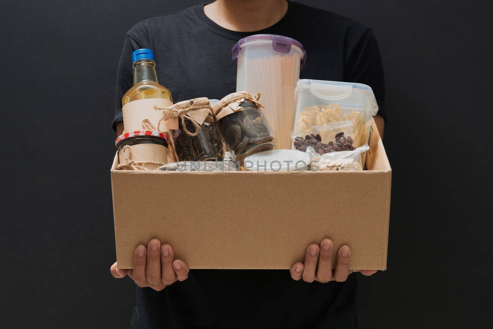 A man holding a donation box of different products on dark background by makidotvn