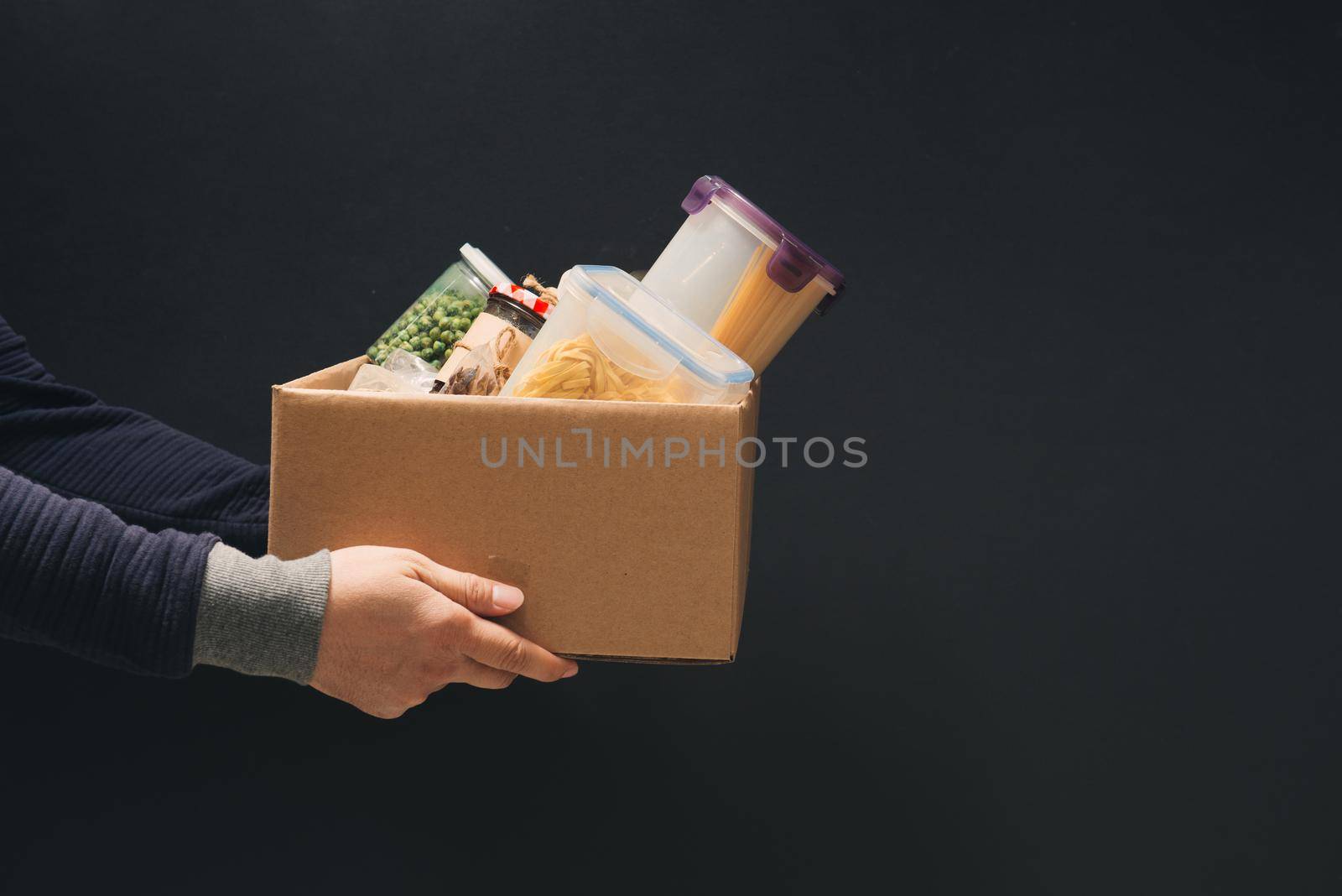 A man holding a donation box of different products on dark background by makidotvn