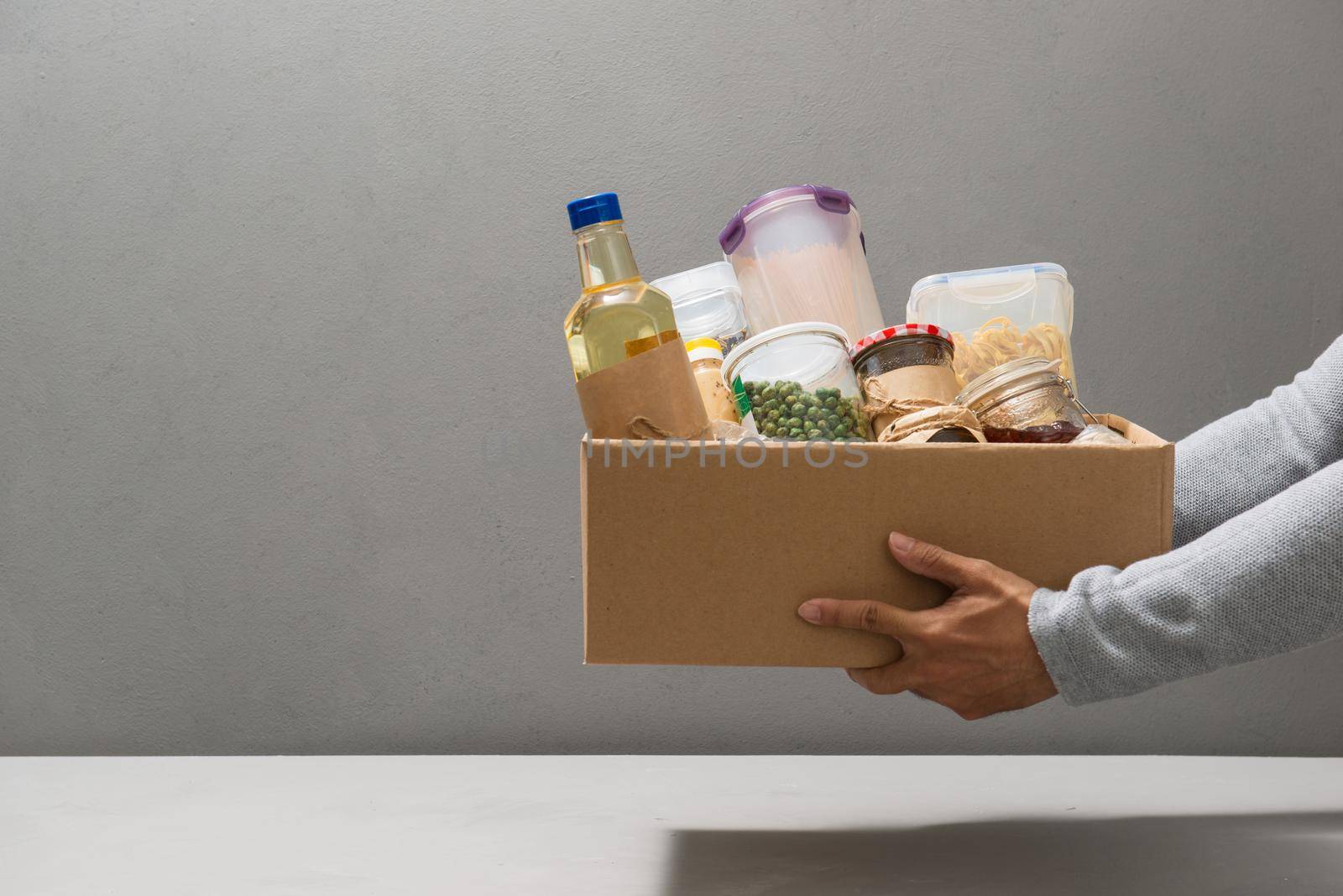 Volunteer in gloves holding food in a donation cardboard box with various food.  by makidotvn