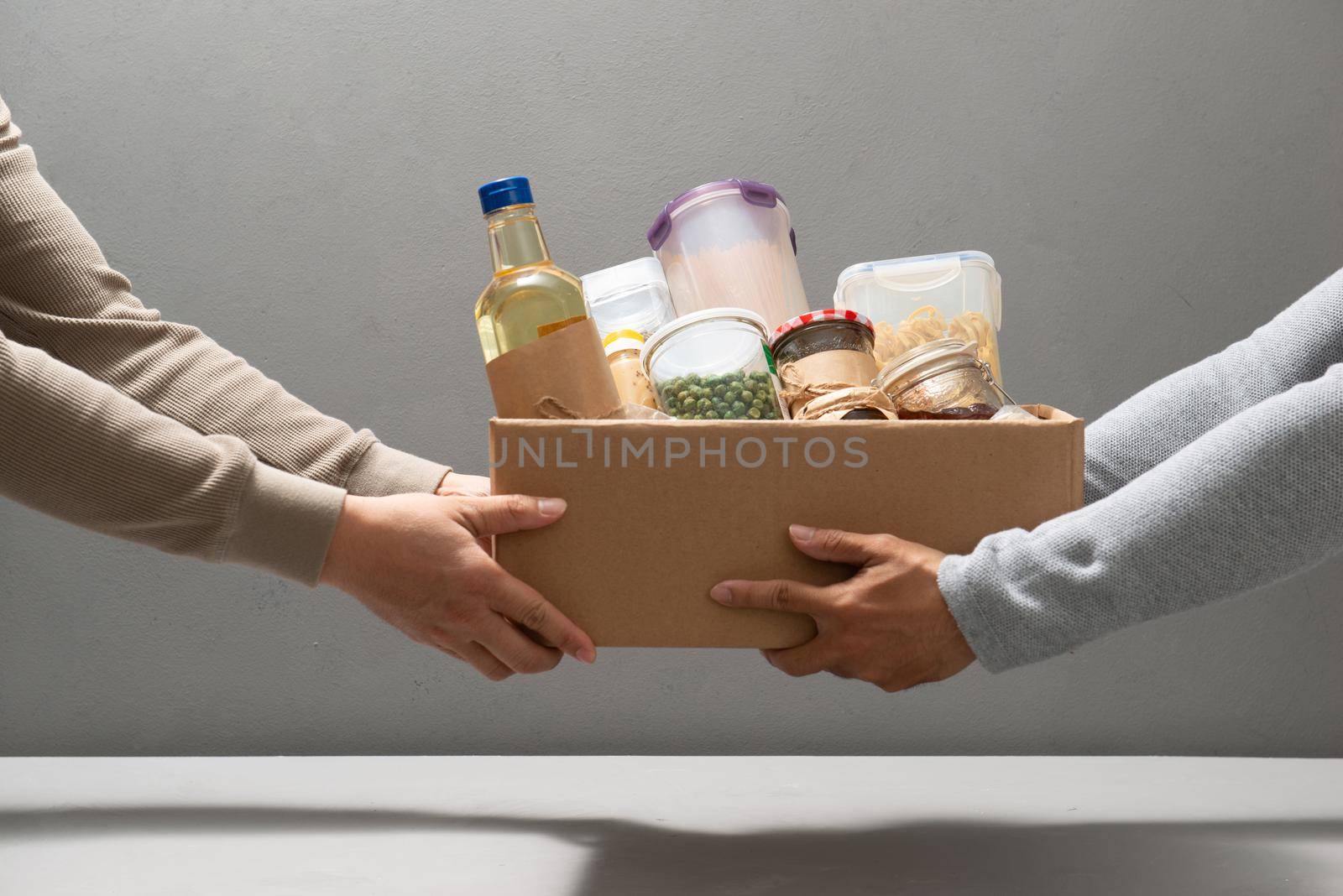 Volunteers with donation box with foodstuffs on grey background