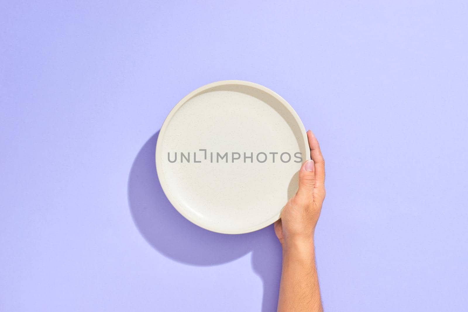 Male hand holding white plate, isolated on lilac background