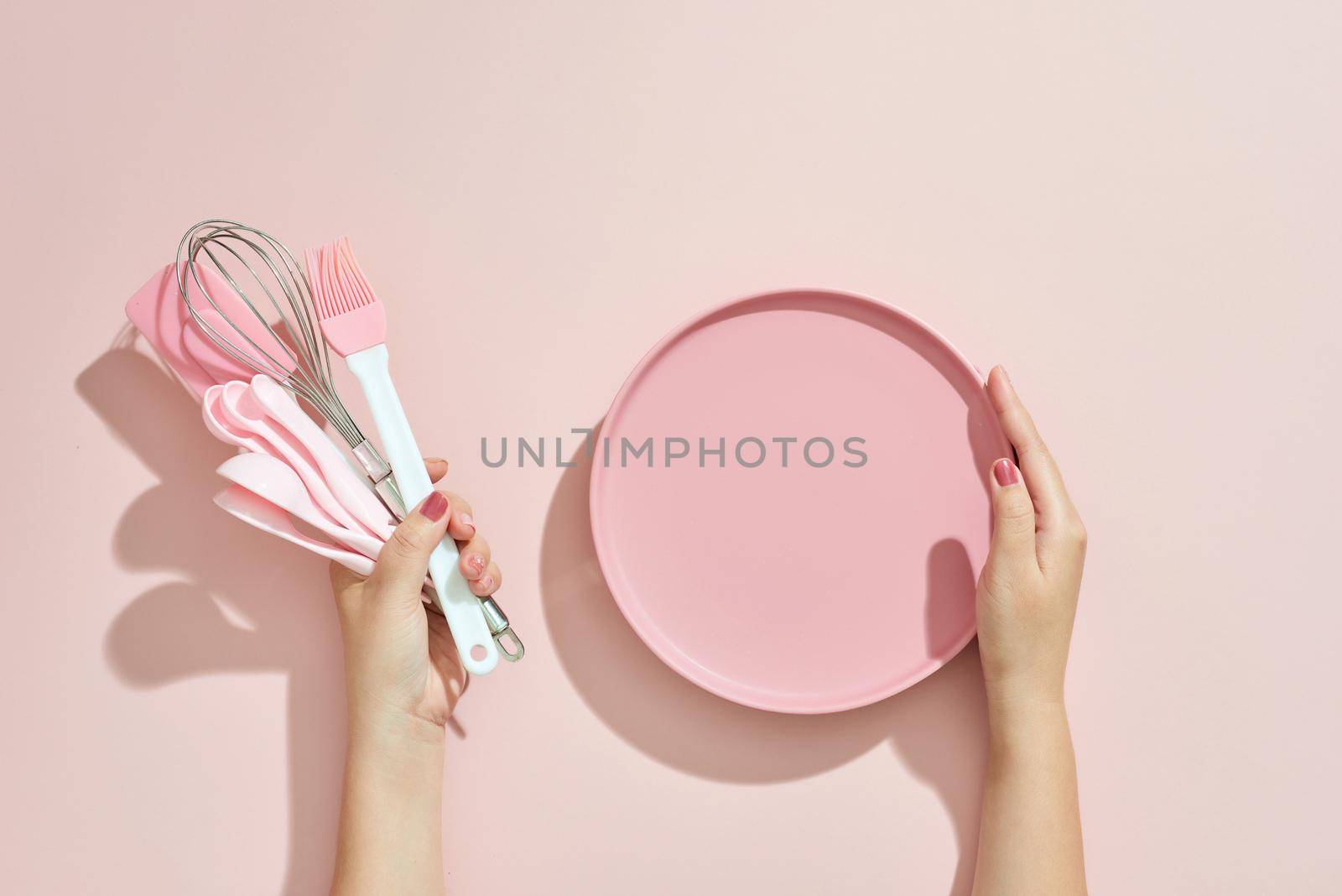 Woman hand holding kitchen utensils on pink background. Baking tools by makidotvn