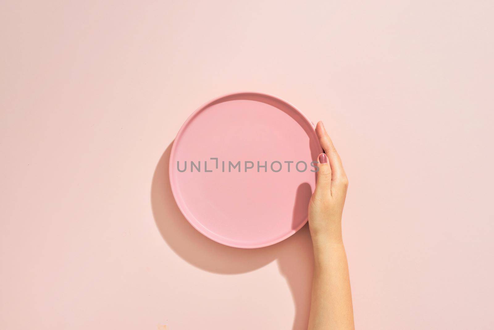 A female hands hold a empty(blank) pink dish(plate) on pink table(desk) by makidotvn