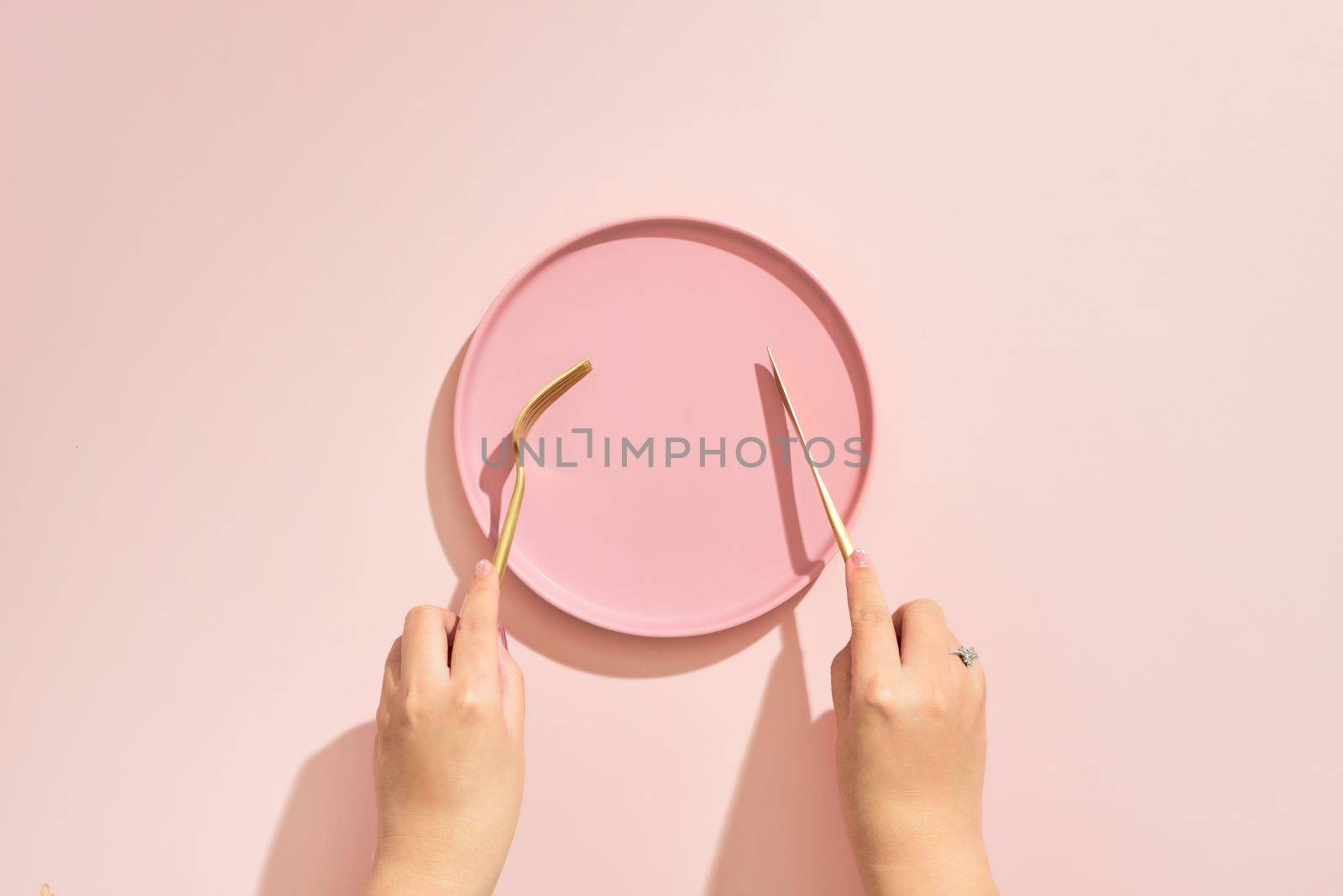 Hands hold a fork and knife over plate on pink background