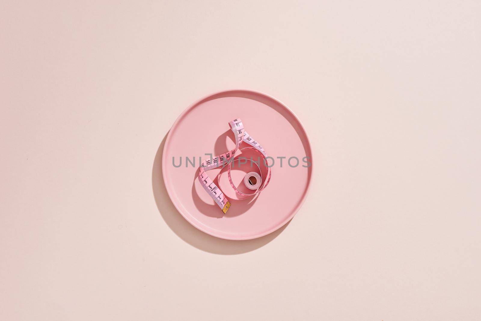 Measuring tape in empty plate on pink table by makidotvn