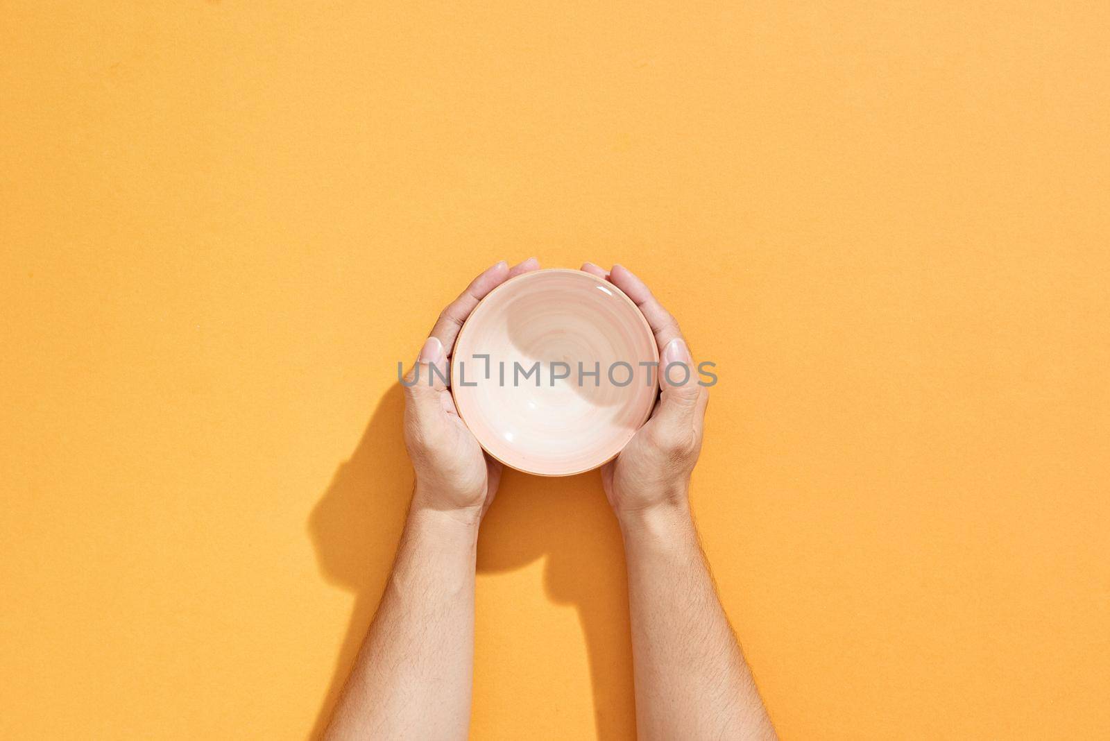 Man holds an empty bowl in his hands over orange