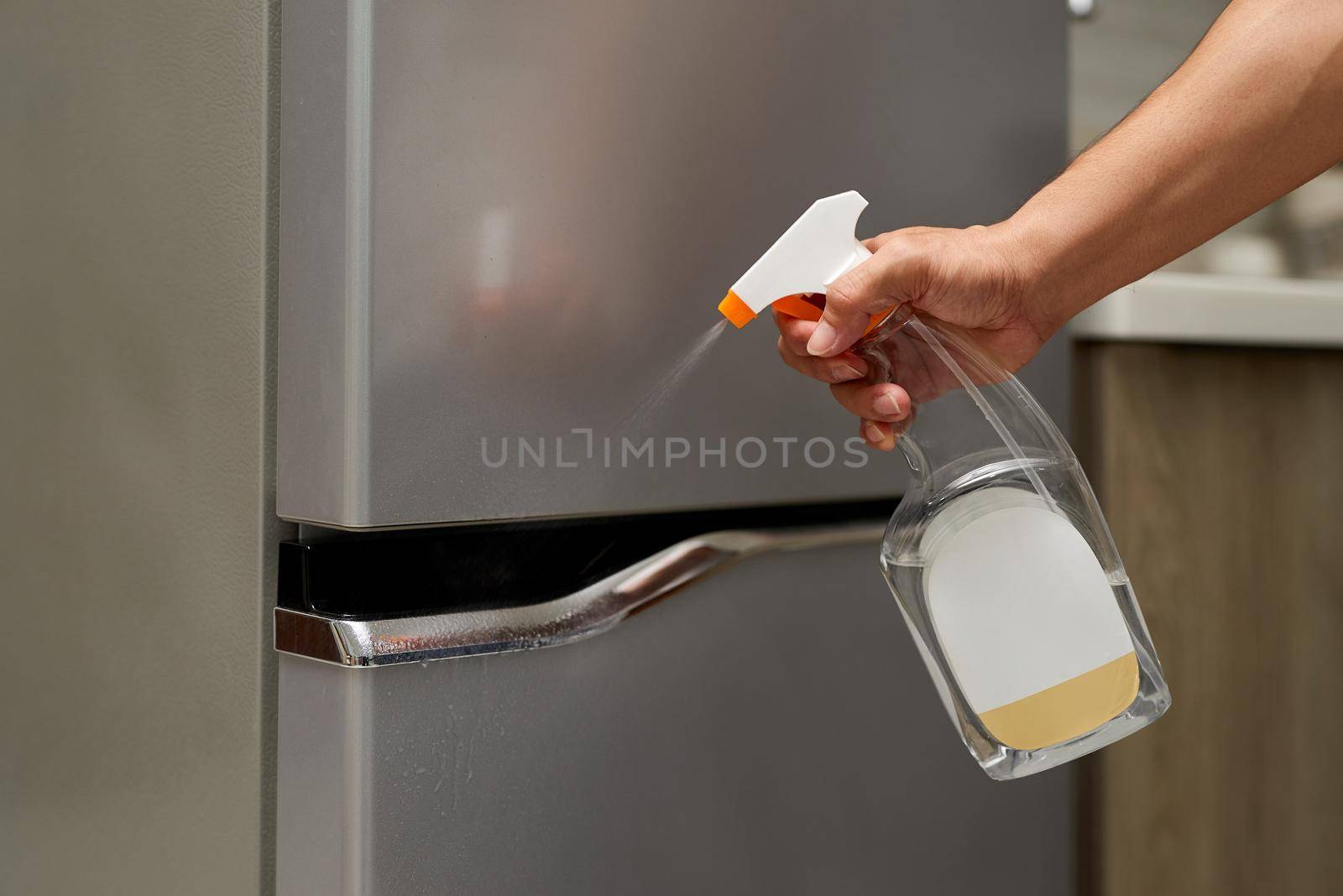 Hand hold bottle alcohol spraying the handle of the fridge door. by makidotvn
