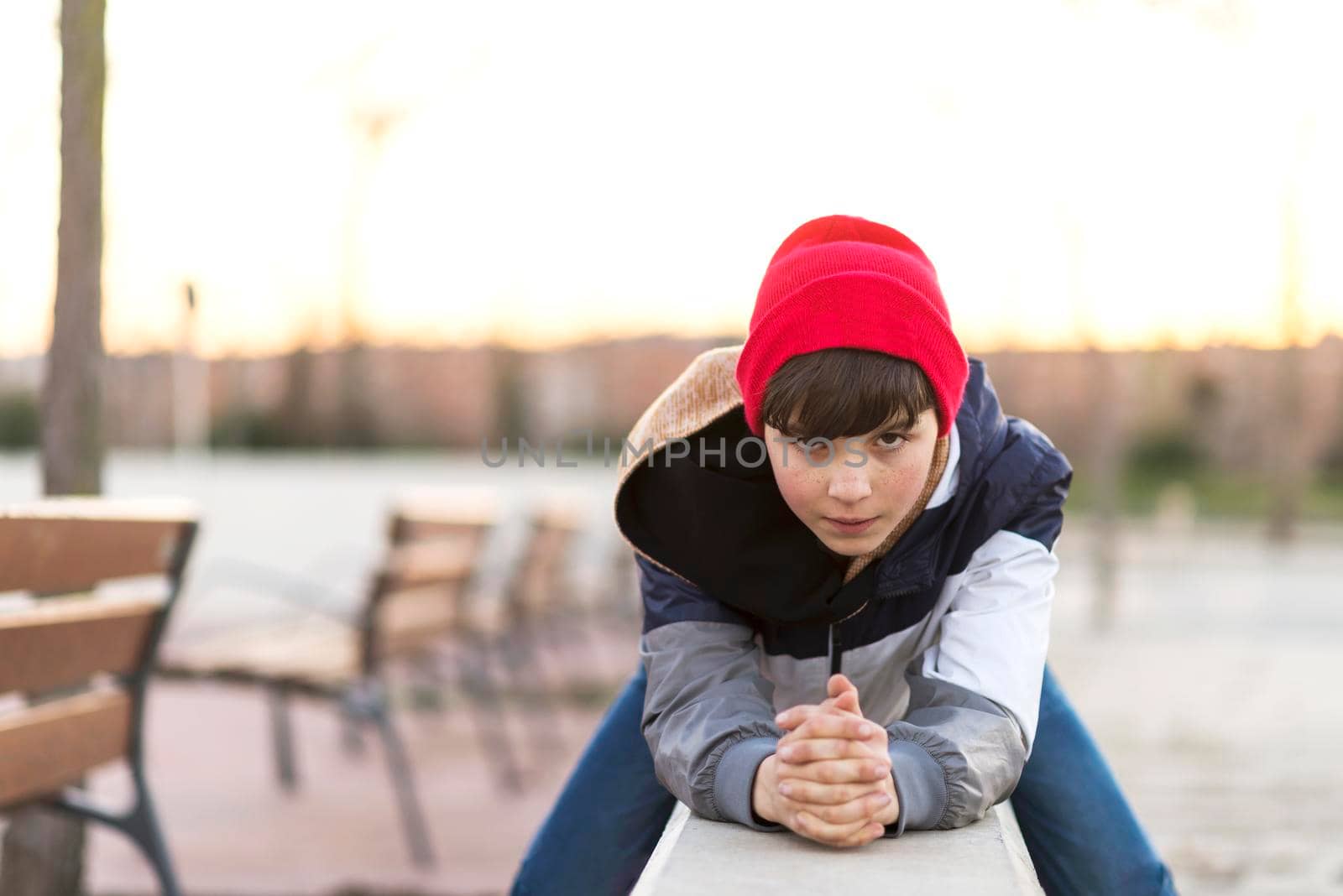 Stylish teenager sitting on a fence in a city park