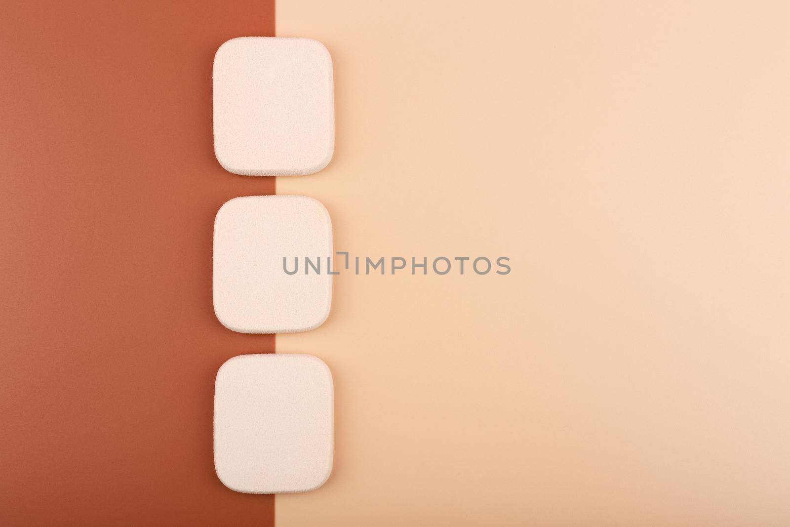 Top view of three square shaped make up sponges on beige and brown backgrounds. Concept of make up and matching foundation for different skin tones