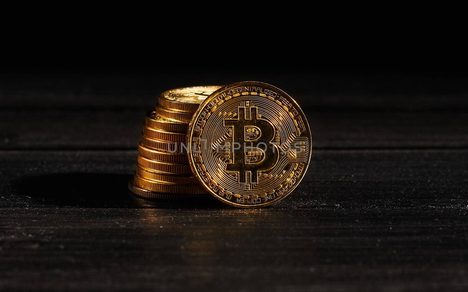 Leader in cryptocurrency bitcoin BTC on a top of coins against black wooden surface. Closeup golden coin with bitcoin logo. Stack of decentralized digital currency. Crypto payment. Electronic money