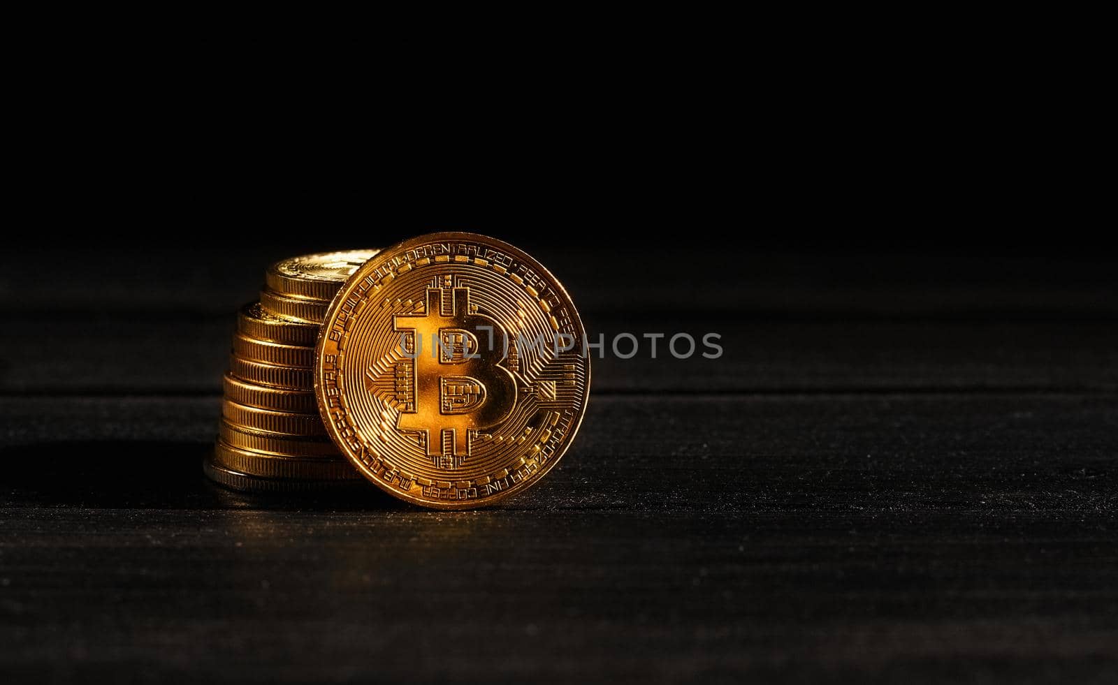 Leader in cryptocurrency bitcoin BTC on a top of coins against black wooden surface. Closeup golden coin with bitcoin logo. Stack of decentralized digital currency. Crypto payment. Electronic money