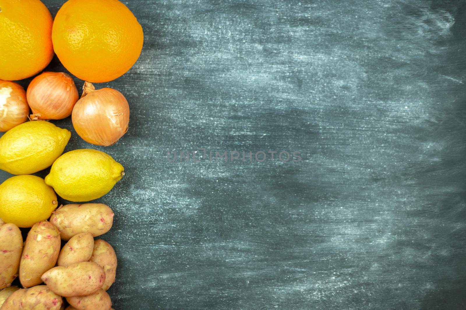 Flat lay of multi-colored raw vegetables on a black background, food frame. Local foods for healthy cooking. potatoes, lemon, orange, onions. Clean food. Top view. Left orientation. Copy space