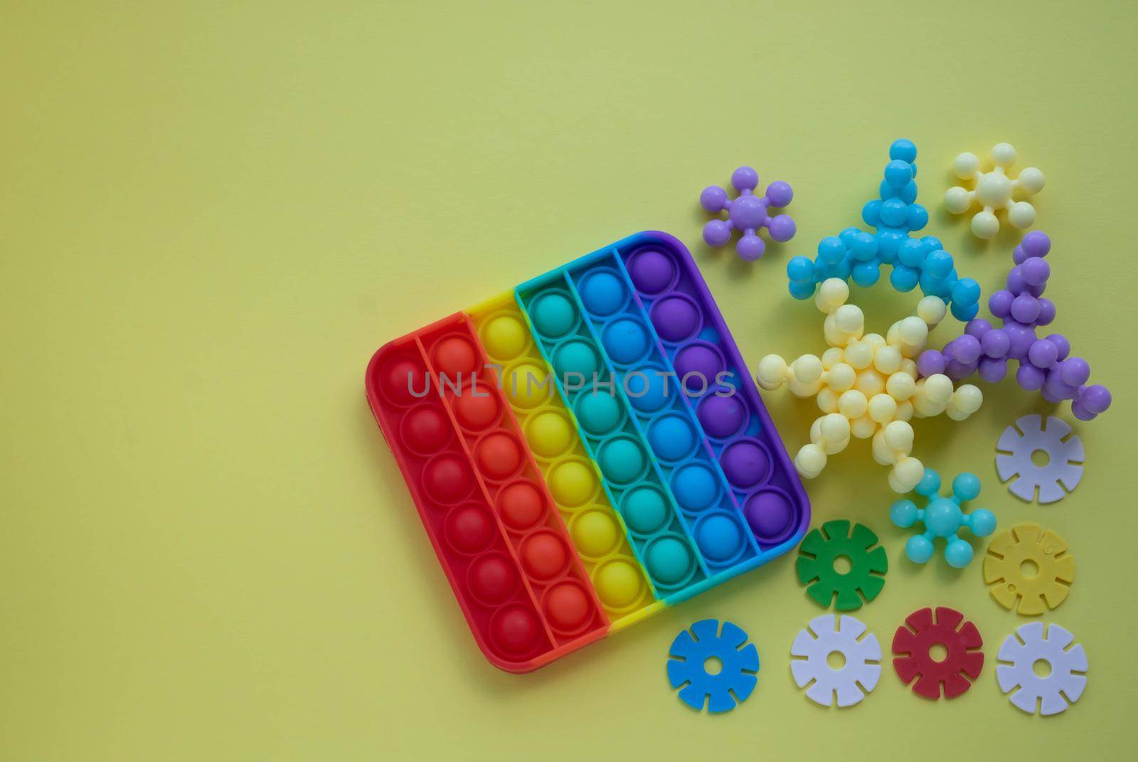 A rainbow toy and puzzles lie on a yellow background. Blue and Orange Funny Interactive Anti-Stress Silicone Toys. Pop it. Space for your text.