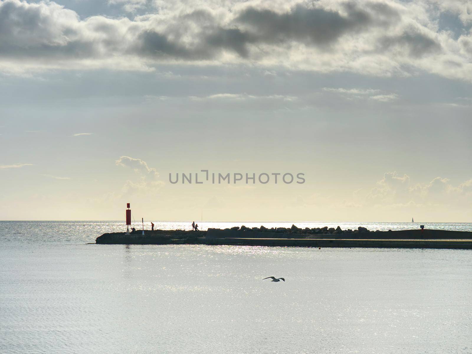 Stony pier or mole with fishermen, small lighthouse at the ond of  promenade.