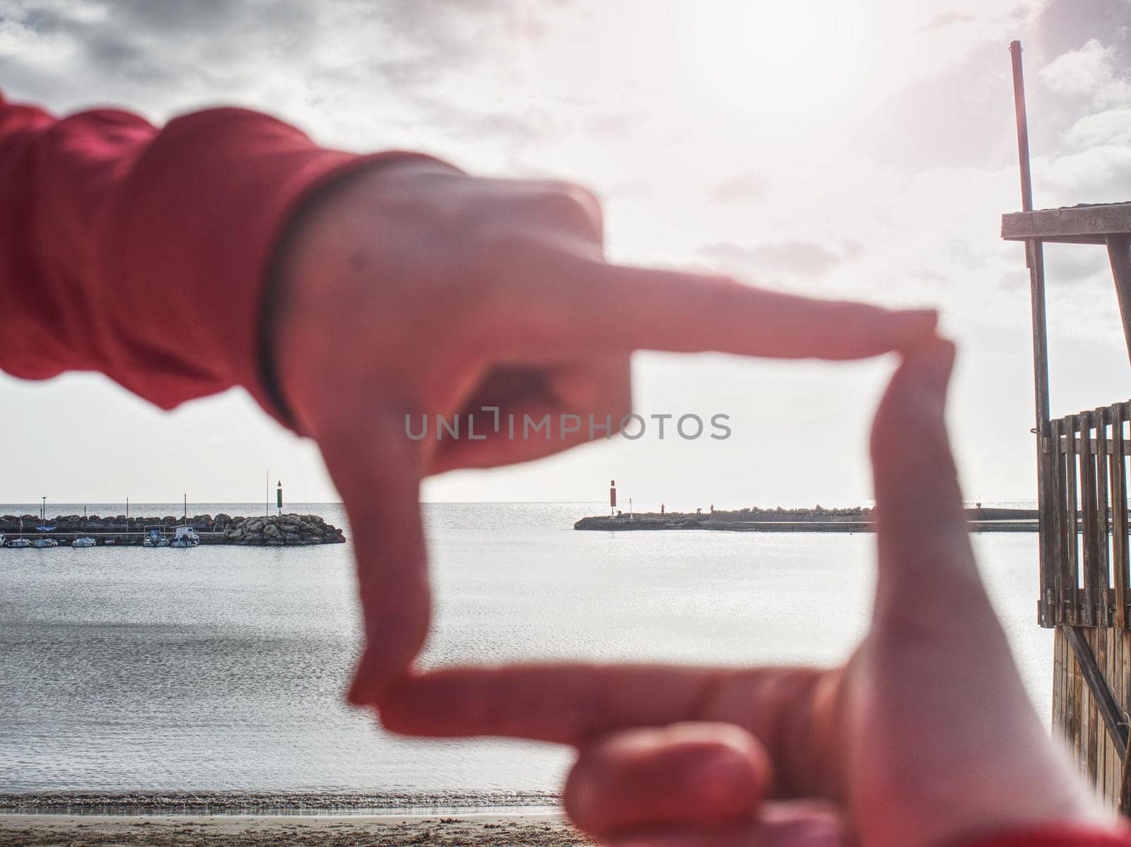 Close up girl hands make frame gesture. Afternoon sun above stony pier of sea.  Sunny spring day with clm water level in bay.