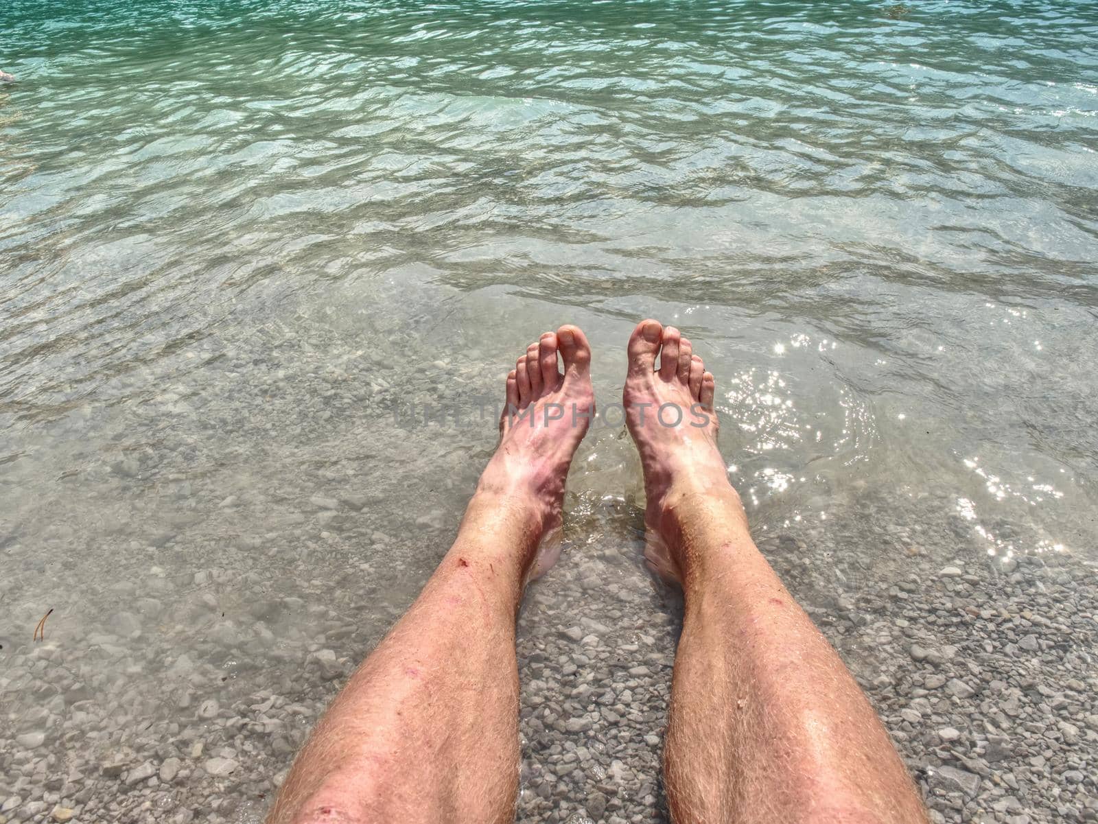 Hairy strong male legs are cooling in cold water of mountain lake. Green blue cold water of kaje in Dolomiti.